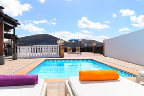 Ein Schwimmbecken mit Liegestühlen und Handtüchern, ein weißer Zaun und ein Berg im Hintergrund.