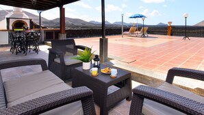 Un espace extérieur aménagé avec des meubles en osier, une table agrémentée d’une plante et de boissons, et offrant une vue sur les montagnes.