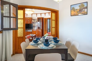 A dining area with a table set for four, wooden cabinets, a television, and a painting on the wall.