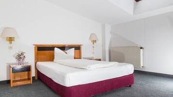 A hotel room with a bed, two bedside tables with lamps, a radiator, and a skylight.