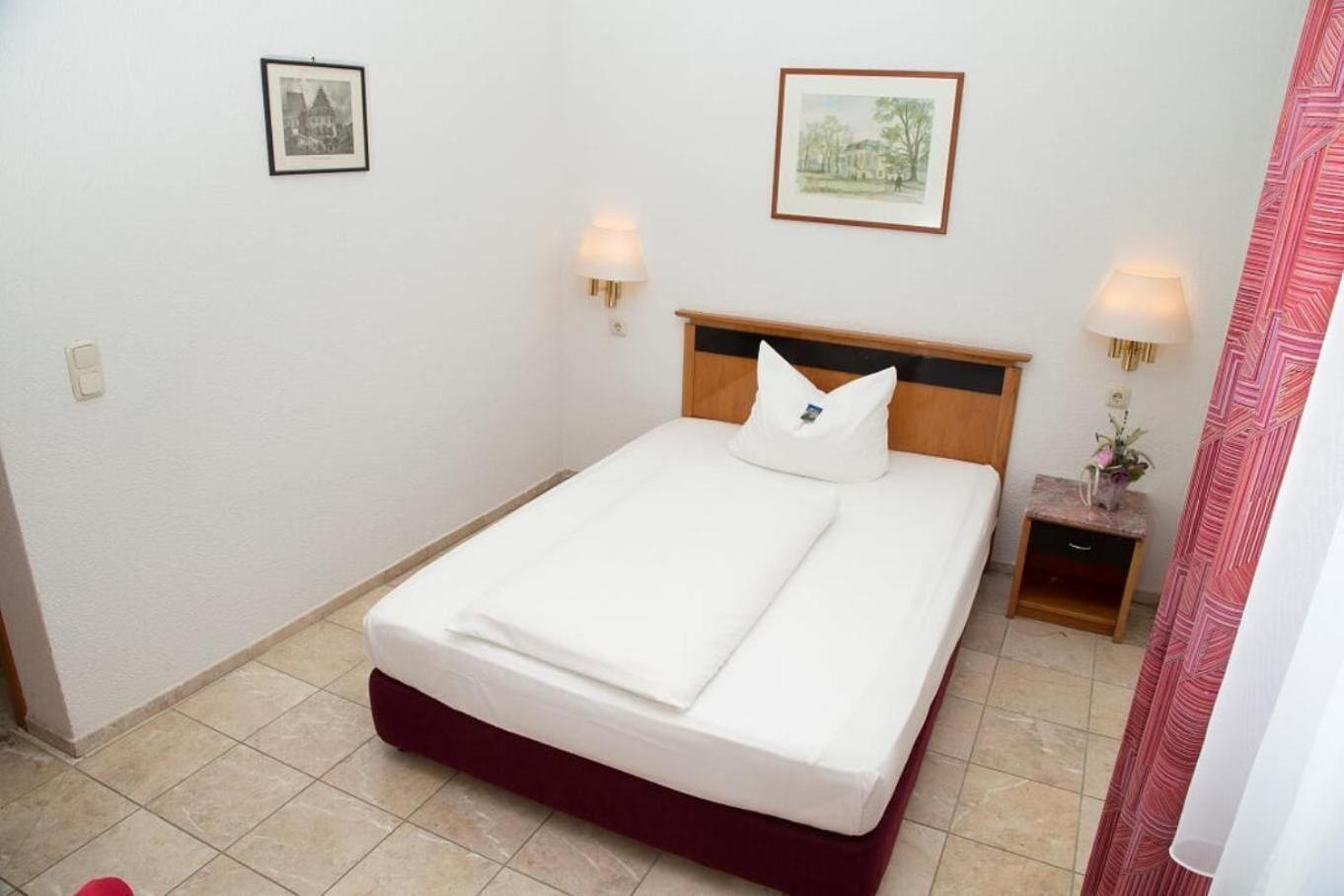 A hotel room with a single bed, two bedside tables, and two wall-mounted lamps.