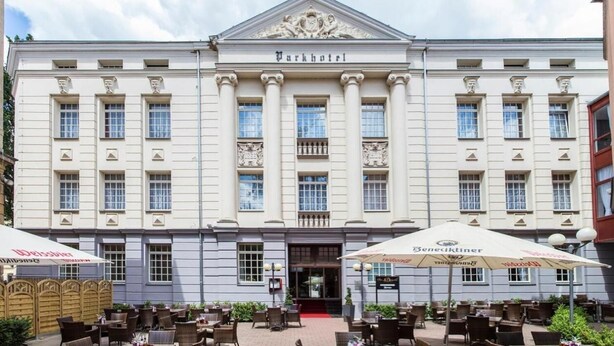 Un edificio grande de estilo clásico con el nombre "Parkhotel" en la fachada. Presenta un diseño simétrico con columnas y una entrada central.