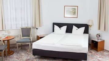 Hotelkamer met een tweepersoonsbed, een stoel, een klein tafeltje, een lamp en een lijst aan de muur.
