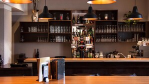 Zona de bar con estantes llenos de botellas y vasos, un mostrador con caja registradora y lámparas colgantes.