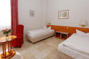 Two single beds with wooden headboards, a nightstand, and a comfortable armchair.