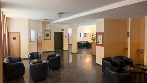 Un vestíbulo de hotel con sillas y mesas de cuero negro, una recepción y cuadros en las paredes.