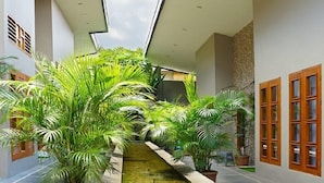 A modern indoor corridor with a central water feature, potted plants, and wooden-framed windows. - IOOVE Tanjung Seminyak Suites (Seminyak)