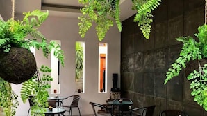 A modern indoor space with hanging green plants, round tables, and wicker chairs. - IOOVE Tanjung Seminyak Suites (Seminyak)
