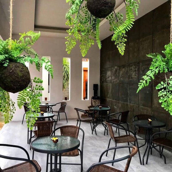 A modern indoor space with hanging green plants, round tables, and wicker chairs. - IOOVE Tanjung Seminyak Suites (Seminyak)