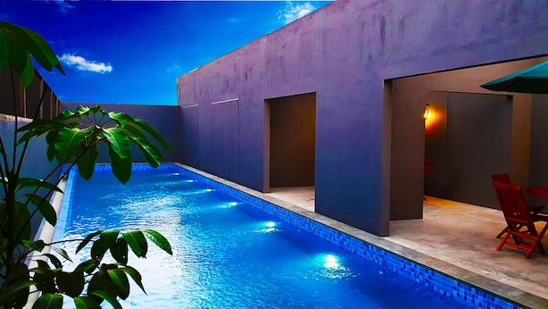 A modern outdoor pool area with a clear blue sky, a pool with blue lighting, and red chairs. - IOOVE Tanjung Seminyak Suites (Seminyak)