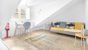 Un dormitorio estilo loft moderno con techo inclinado, un área de comedor con mesa y sillas, un sofá con cojines y una pequeña mesita auxiliar.