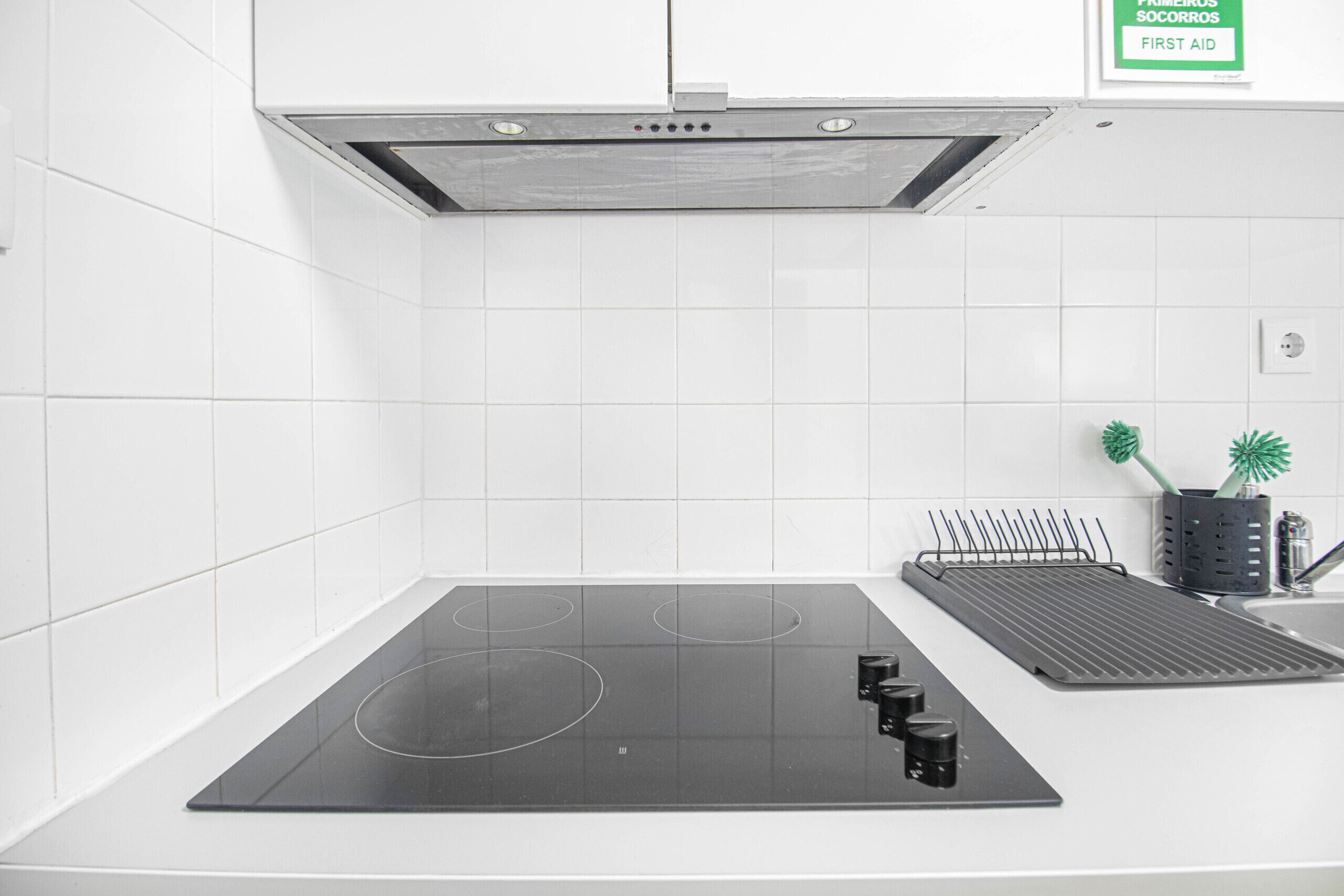 A kitchen with a black induction cooktop, a stainless steel range hood, and a black drying rack.