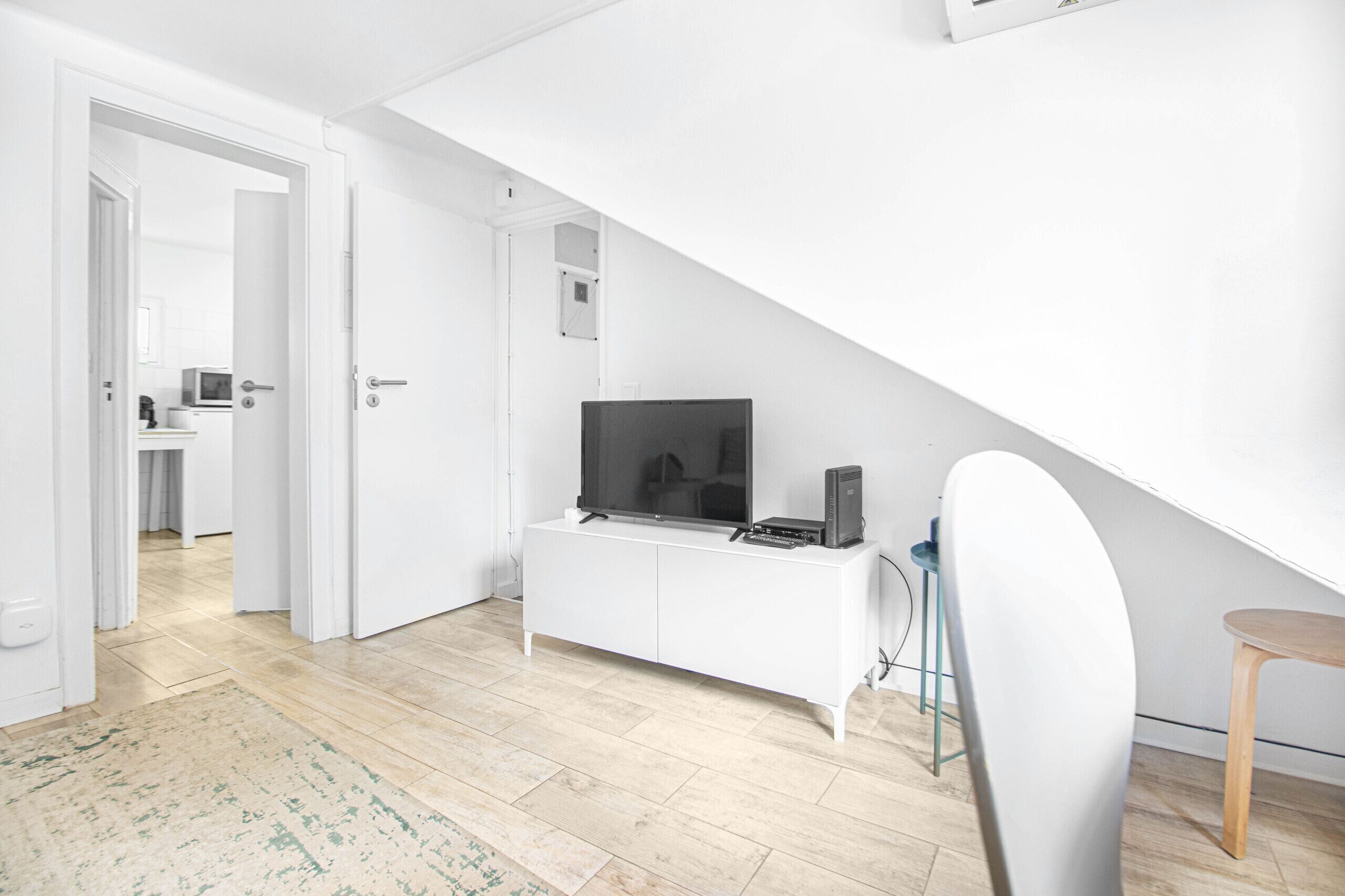 Een moderne woonkamer met een witte entertainmentkast, een flatscreen-televisie en een eethoek met een stoel en tafel.