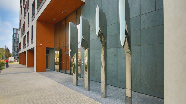 Een modern gebouw met een tegelpad en grote, reflecterende kolommen.