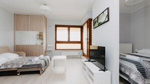 Een moderne slaapkamer met een bed, een televisie, een bureau en een raam met jaloezieën.