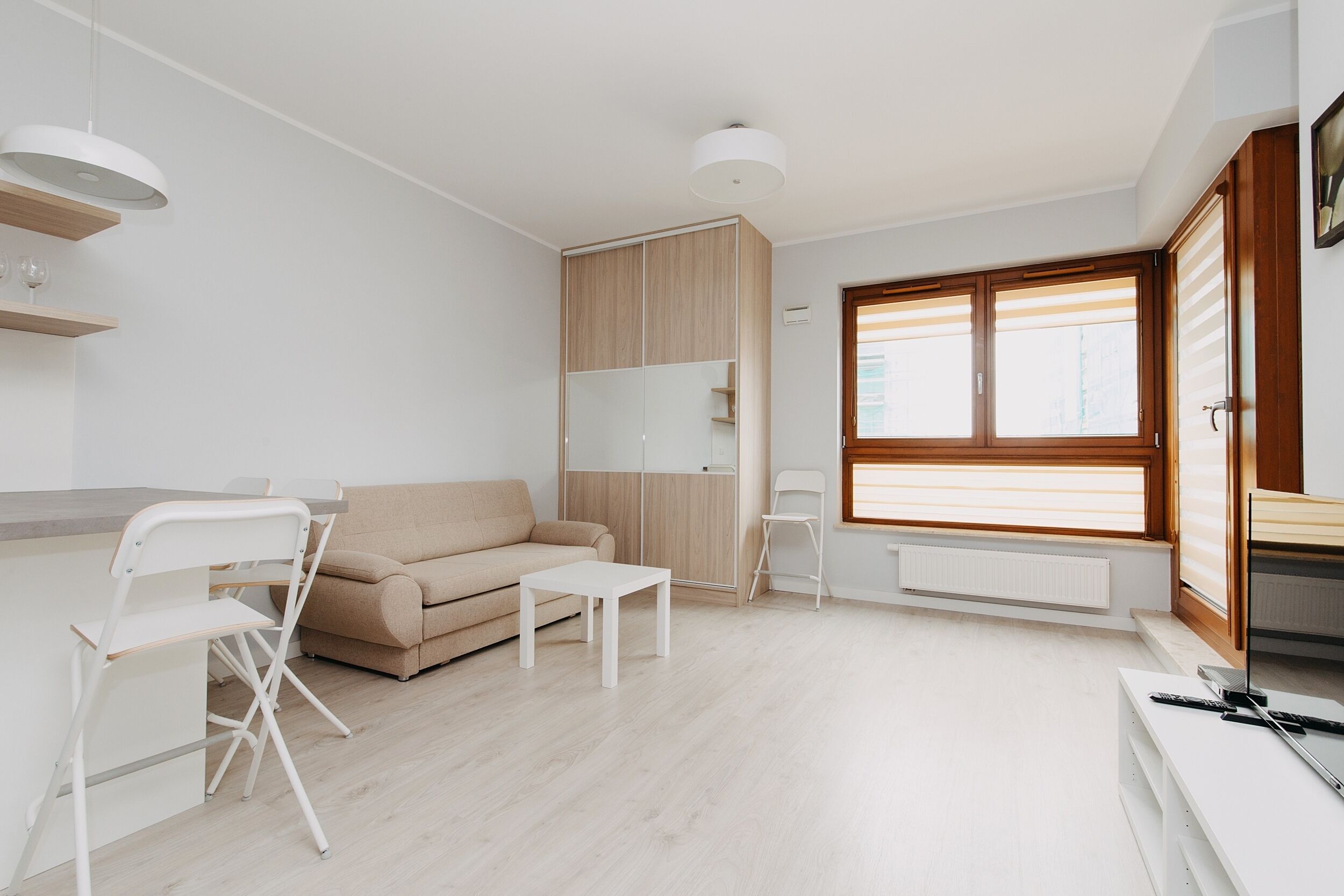 A modern, minimalist living space with a sofa, a small table, a white chair, and a wooden cabinet.
