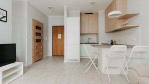 Een moderne keuken met witte kasten, een houten deur, een televisie en een bar met witte stoelen.