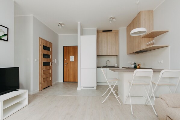 A modern kitchen with white cabinetry, a wooden door, a TV, and a bar area with white chairs.