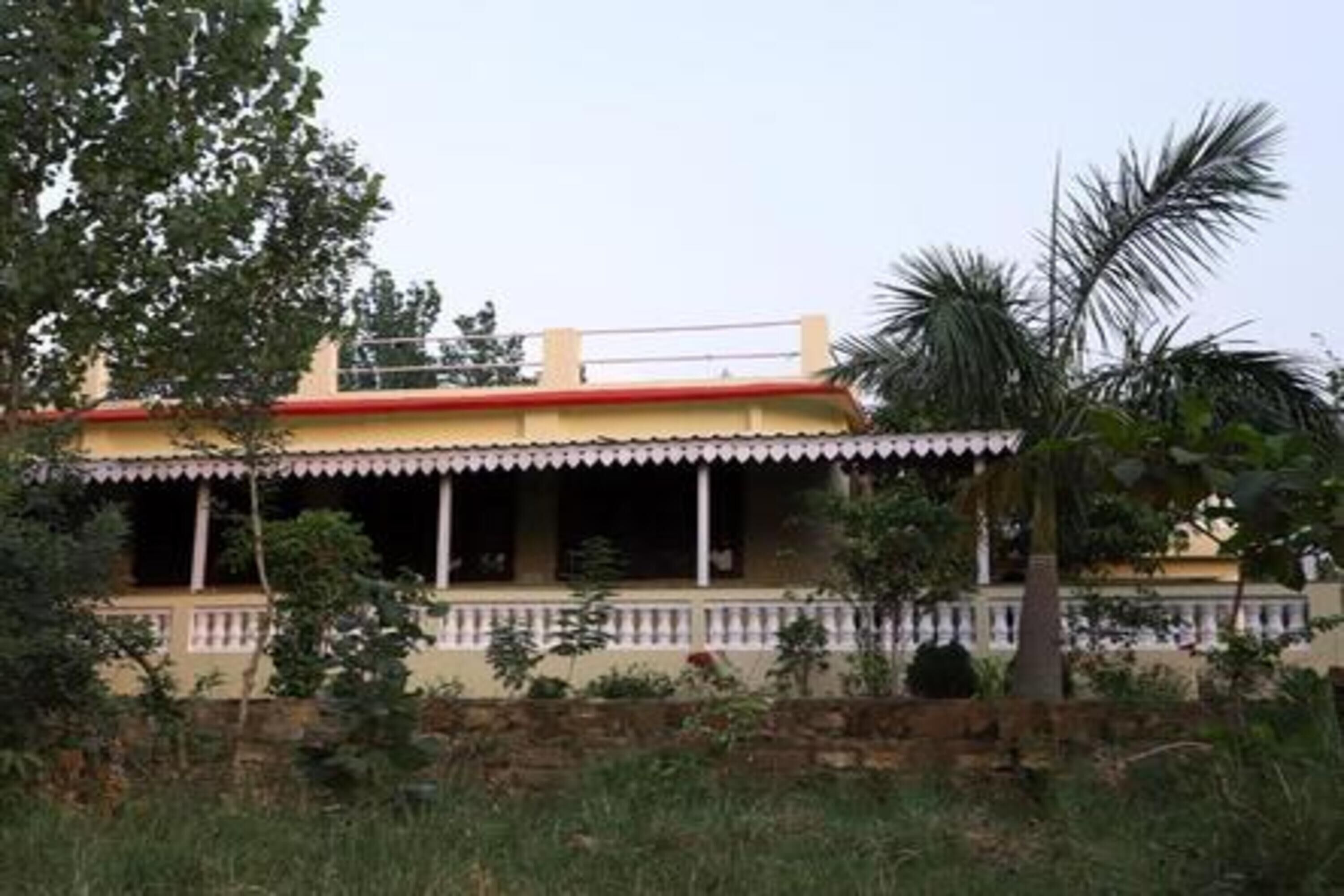 A two-story building with a red roof and white trim. It has a balcony with railings and is surrounded by greenery.
