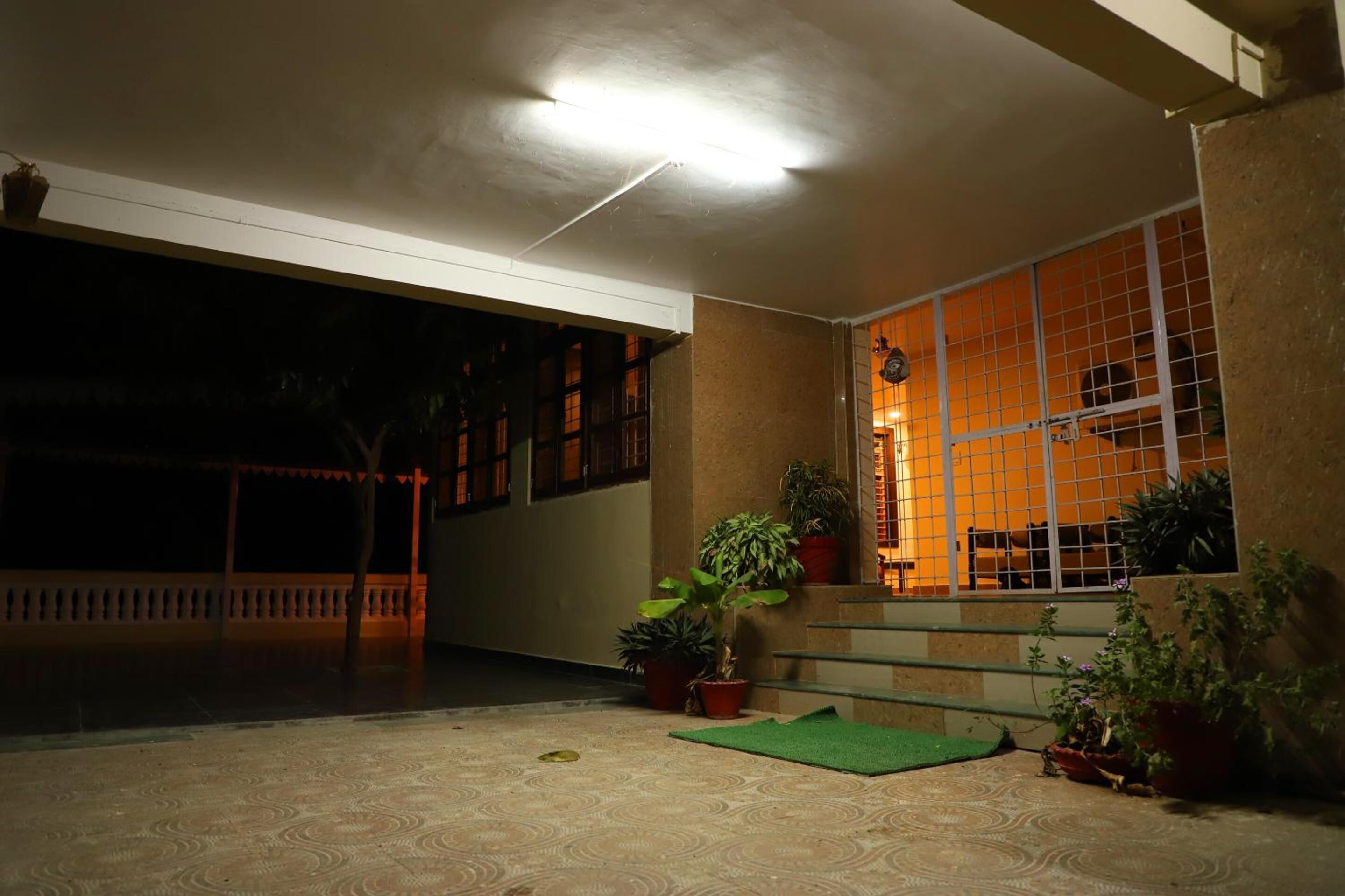 Un patio tenuemente iluminado con una escalera que conduce a una habitación, plantas en macetas y suelo de baldosas.