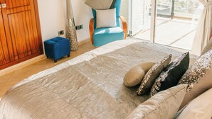 A bedroom with a large bed, a blue chair, a wooden wardrobe, and a view of the outside. - Sea La Vie – Ocean-View Villa with Private Pool, Sunset Terrace and Privacy (Costa Adeje Tenerife)