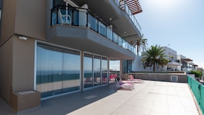 A modern building with large glass windows, a balcony with red chairs, and a palm tree. - Sea La Vie – Ocean-View Villa with Private Pool, Sunset Terrace and Privacy (Costa Adeje Tenerife)