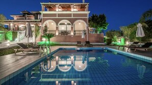 A two-story building with a swimming pool, outdoor seating, and a well-lit patio area. - Amalthia Villa (Zakynthos)