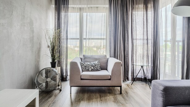 Un salon moderne avec un canapé gris, un ventilateur sur pied et une plante en pot.
