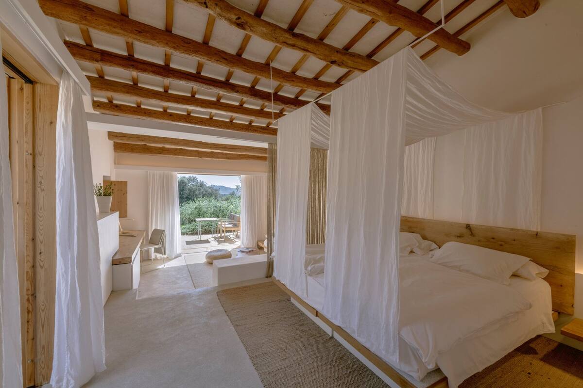 Ein Schlafzimmer mit Holzboden, einem großen Bett, einem Schreibtisch und Blick ins Freie.