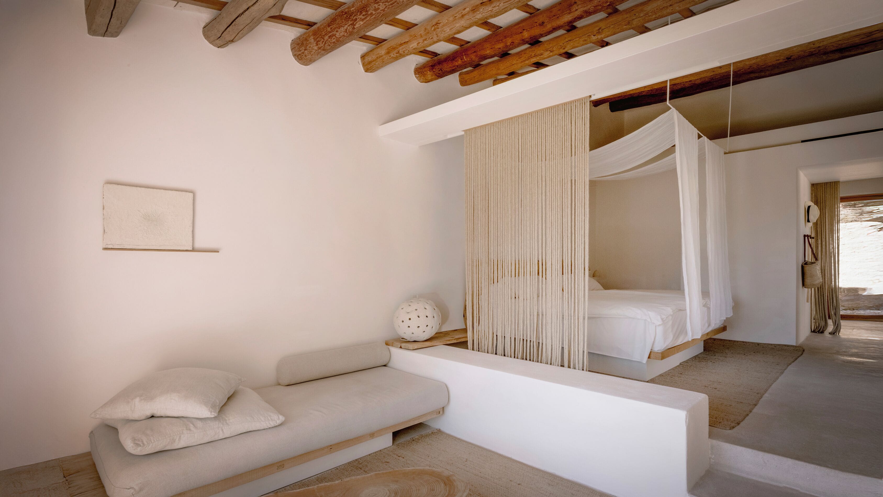 A bedroom with a wooden ceiling, a bed with a canopy, a sofa, and a small decorative item on the floor.