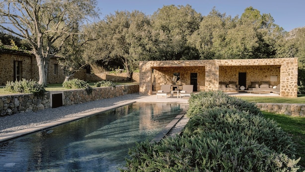 Un edificio de piedra con piscina, mobiliario exterior y un muro de piedra.