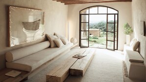 Una habitación amplia con un gran ventanal, un banco de madera, un sofá y un cuadro en la pared.
