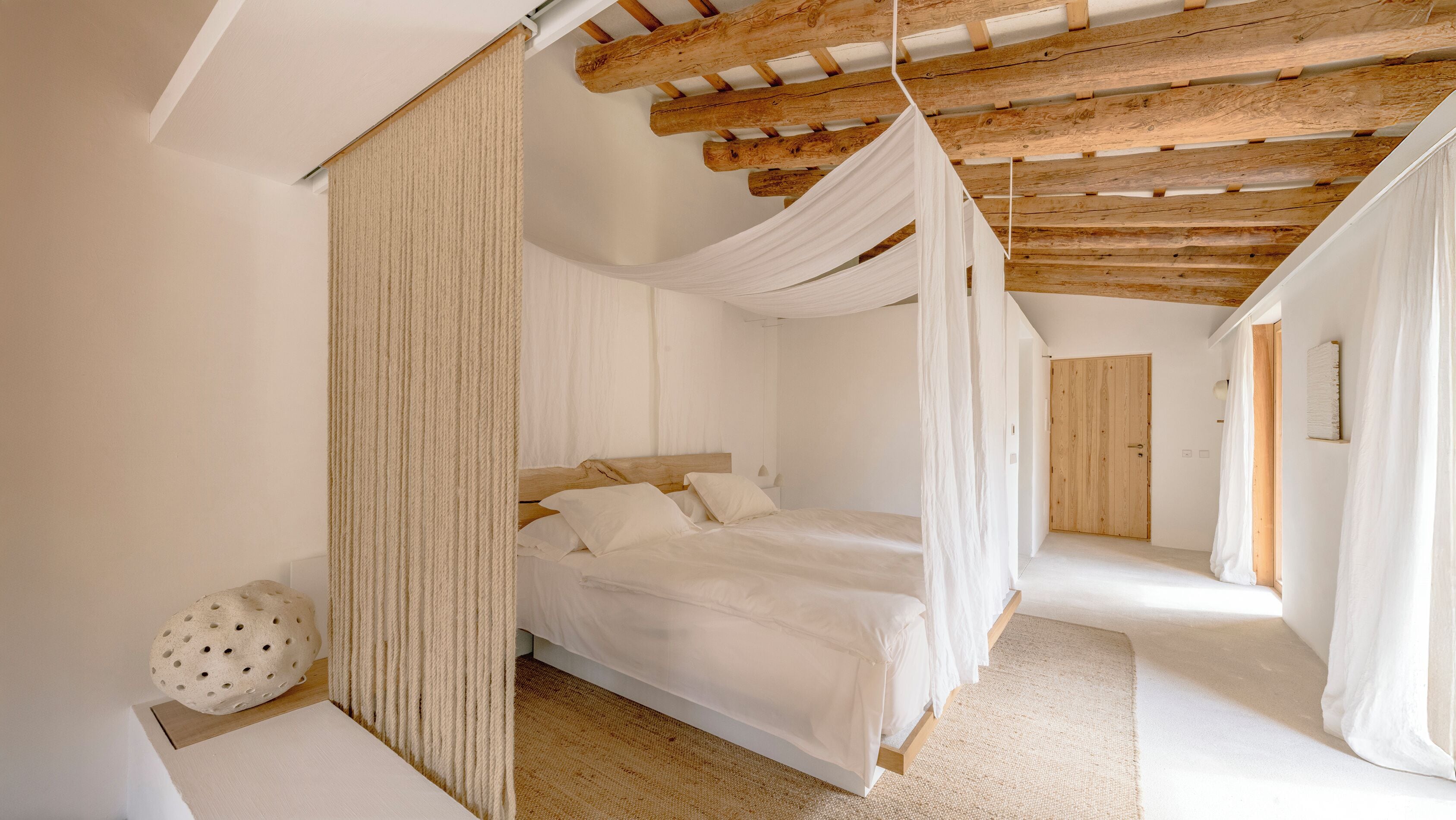 Un dormitorio con techo de madera, cama con ropa de cama blanca y un ventanal grande.
