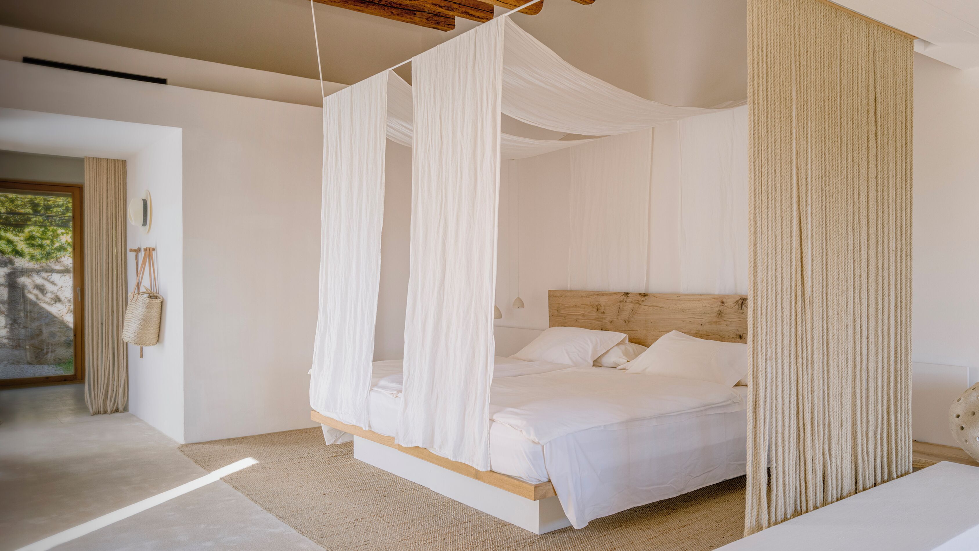 Une chambre spacieuse dotée d’un lit à baldaquin, d’une tête de lit en bois et offrant une vue sur l’extérieur.