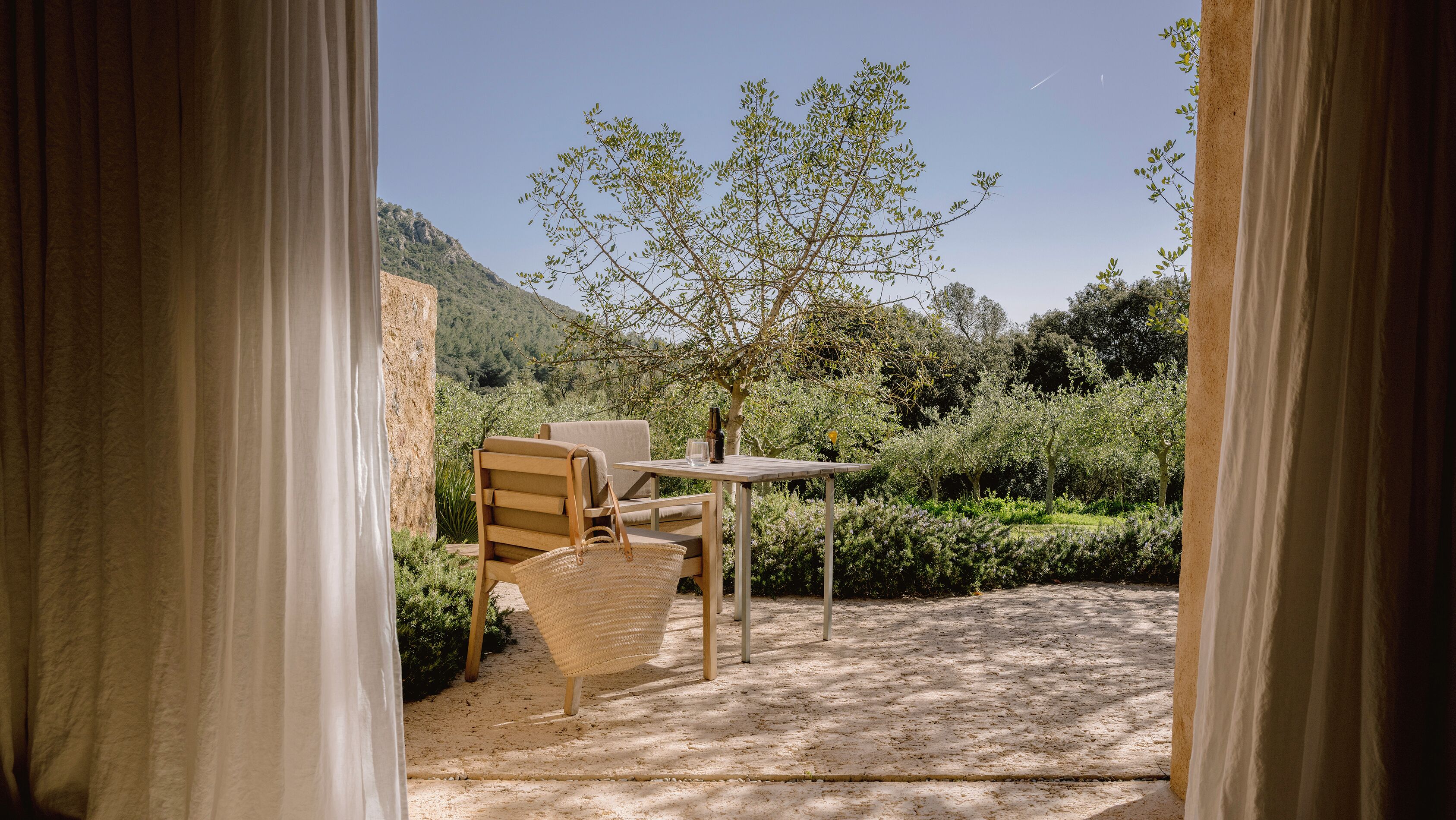 An outdoor seating area with a table and chairs, surrounded by greenery and a view of a hillside.