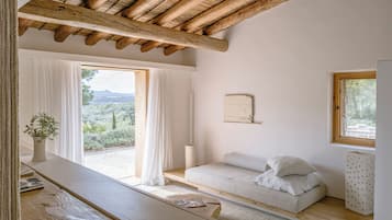 Un dormitorio con techo de madera, una cama con almohadas, una mesita de noche, una ventana con cortinas y vistas al exterior.