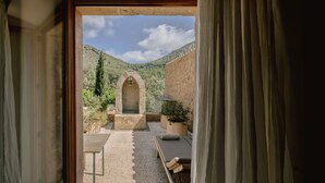 Vista a través de una puerta que muestra un espacio exterior con un banco de piedra, una mesa y una planta en maceta.