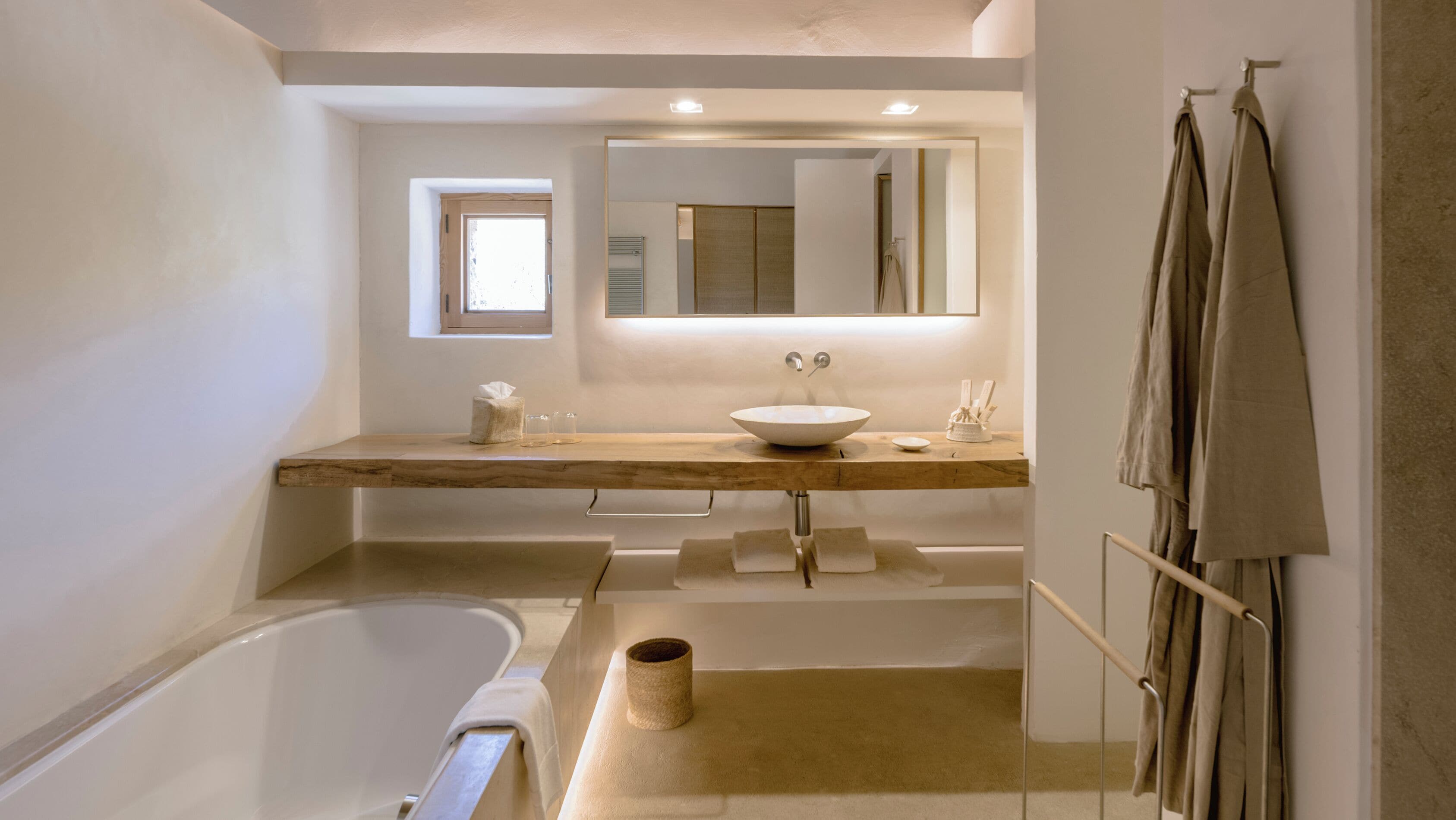 Un baño moderno con una bañera independiente, un espejo grande y un mueble de tocador de madera con lavabo.