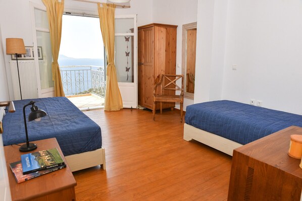 A bedroom with two beds, a wooden chair, a desk with a lamp, and a view of the sea through a balcony. - Private Villa with Breathtaking sea view, Swimming pool, Near the beach (Skaloma, Phokis)