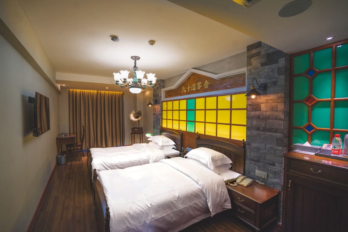A hotel room with two beds, a desk, a chair, a telephone, and a decorative wall with a geometric pattern.