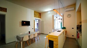 A modern kitchen with a wooden island, a dining area with chairs, a TV mounted on the wall, and a clock on the wall. - Neapolitan Flat B&B (Naples)