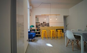 A modern kitchen with wooden countertops, a blue chair, yellow stools, and a dining table with white chairs. - Neapolitan Flat B&B (Naples)