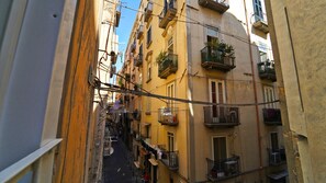 A narrow urban street with buildings on both sides, featuring balconies with plants and laundry hanging out to dry. - Neapolitan Flat B&B (Naples)