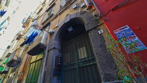 A narrow street with old buildings, a red wall with a sign, and a small plant. - Neapolitan Flat B&B (Naples)