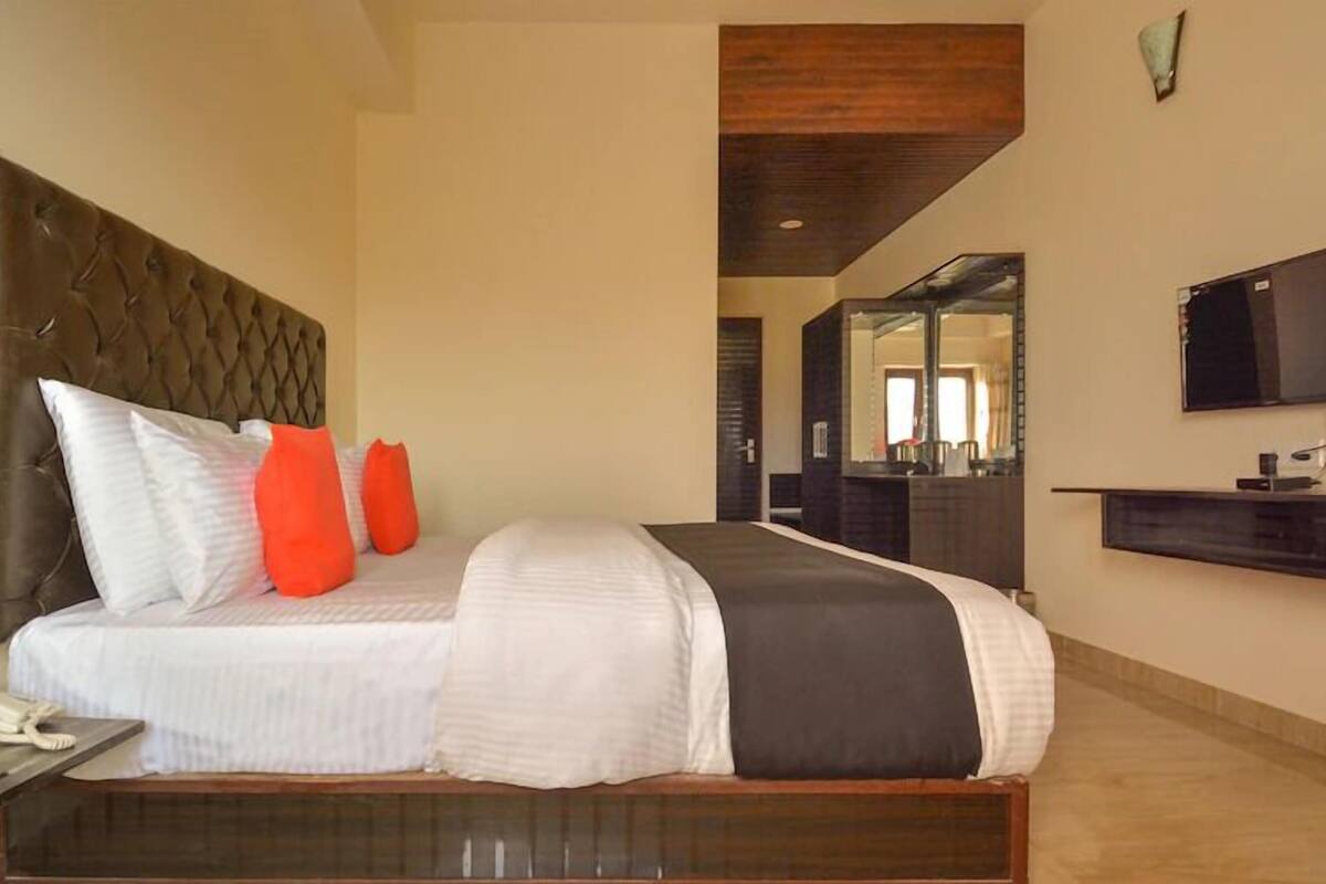 A hotel room with a large bed, a bedside telephone, a flat-screen TV mounted on the wall, and a mirror above the bed.