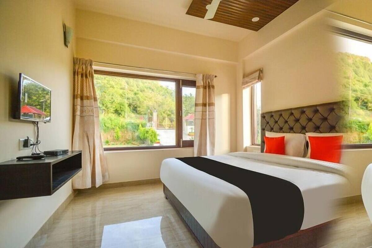 A modern hotel room with a large bed, a flat-screen TV, and a view of greenery outside.