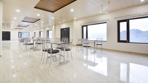 A spacious conference room with tables and chairs, large windows, and a wooden ceiling. - Nakshatra Resort Shimla (Arki)