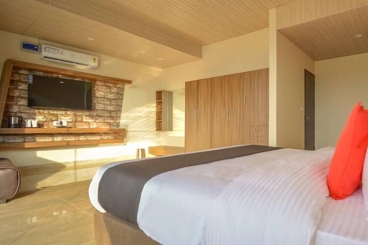 A modern hotel room with a large bed, a flat-screen TV mounted on a stone wall, and a wooden wardrobe.