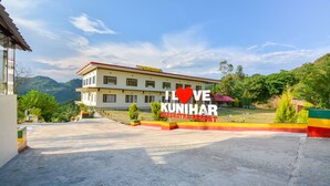 A hotel with a large building, a sign reading "I LOVE KUNIHAR", and a view of mountains in the background. - Nakshatra Resort Shimla (Arki)