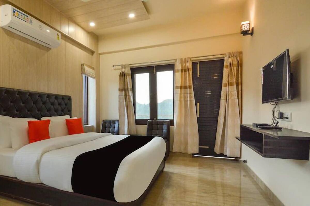 A hotel room with a large bed, a TV, an air conditioning unit, and a window with curtains.